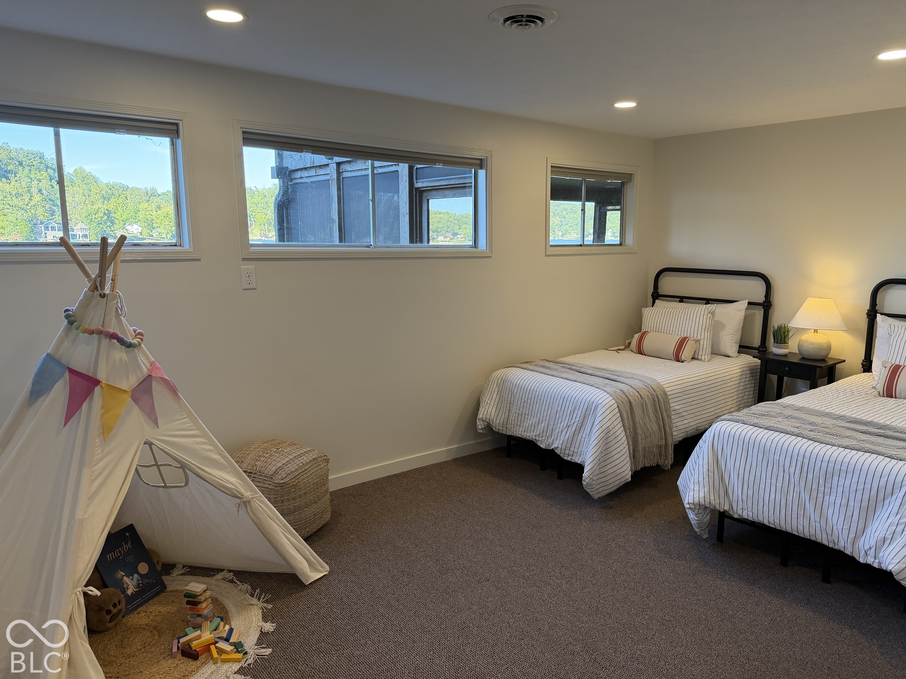 Bedroom with two twin beds and a play teepee, with water visible through the windows.