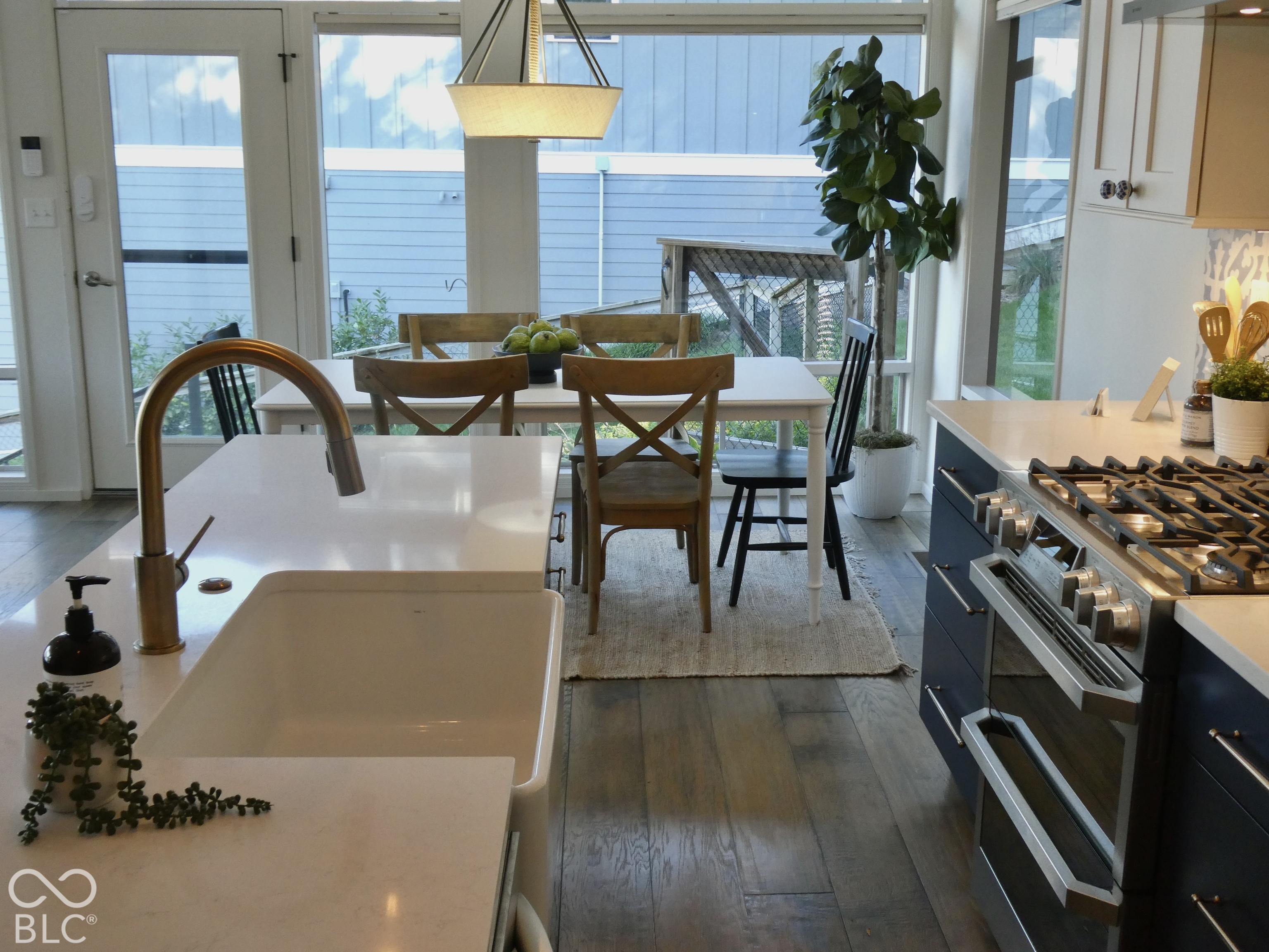 Kitchen with a white island, dark blue cabinetry, stainless range, and dining table by large windows.