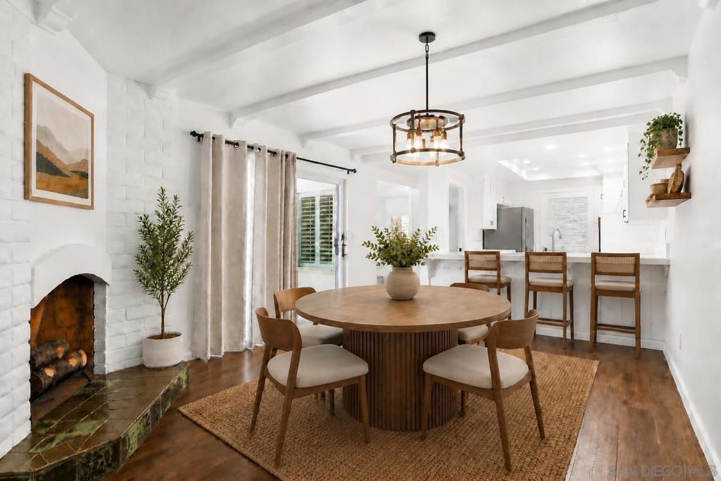 Dining room with a round wood table, white brick fireplace, and open kitchen.