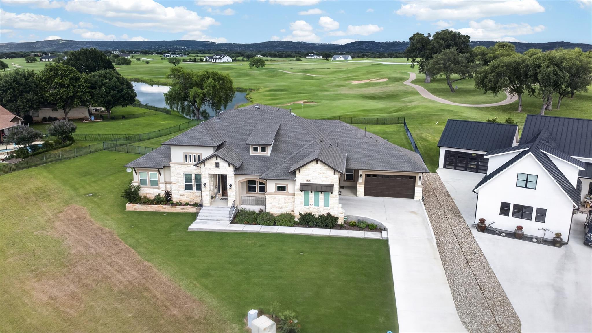 Aerial view of a stone-front home beside a golf course and pond.