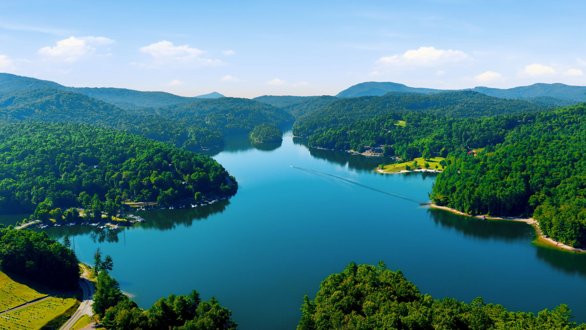 Aerial view of a forested lake and mountain ridges, with homes along the shore.