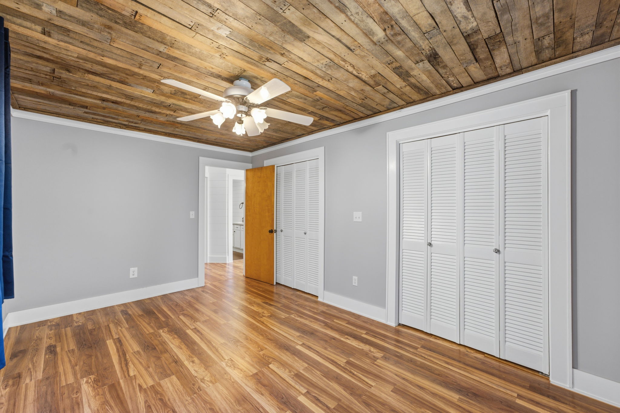 Empty bedroom with a rustic wood-plank ceiling, hardwood floors, and white louvered closet doors.