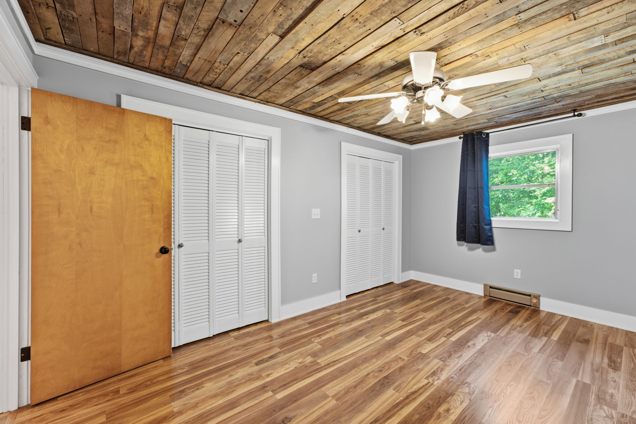 Vacant bedroom with a rustic plank ceiling, wood floors, closet doors, and a window.