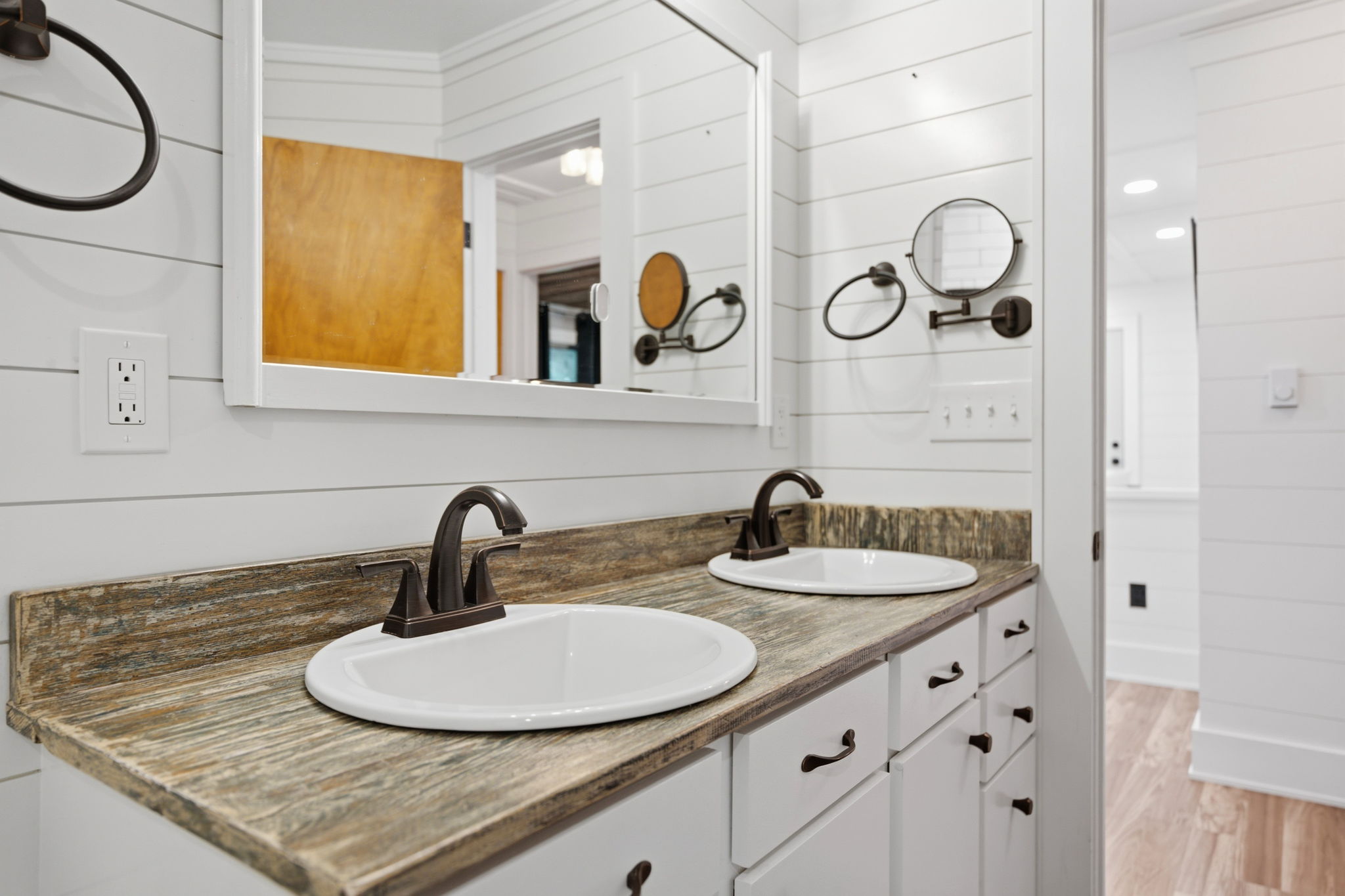 Bathroom double vanity with two white sinks, dark faucets, and a weathered wood countertop.