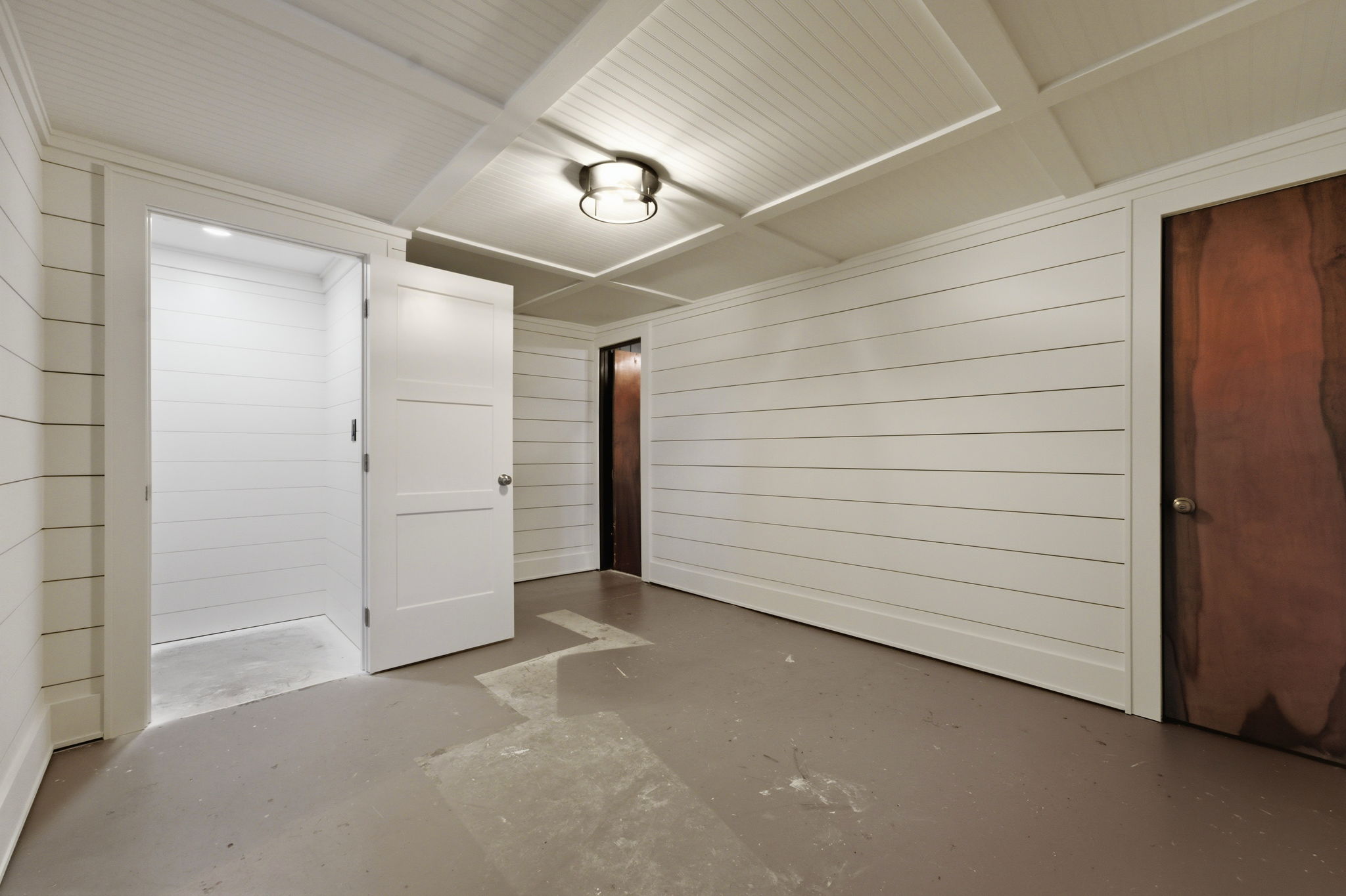 Vacant garage with white paneled walls, concrete floor, and several doors.