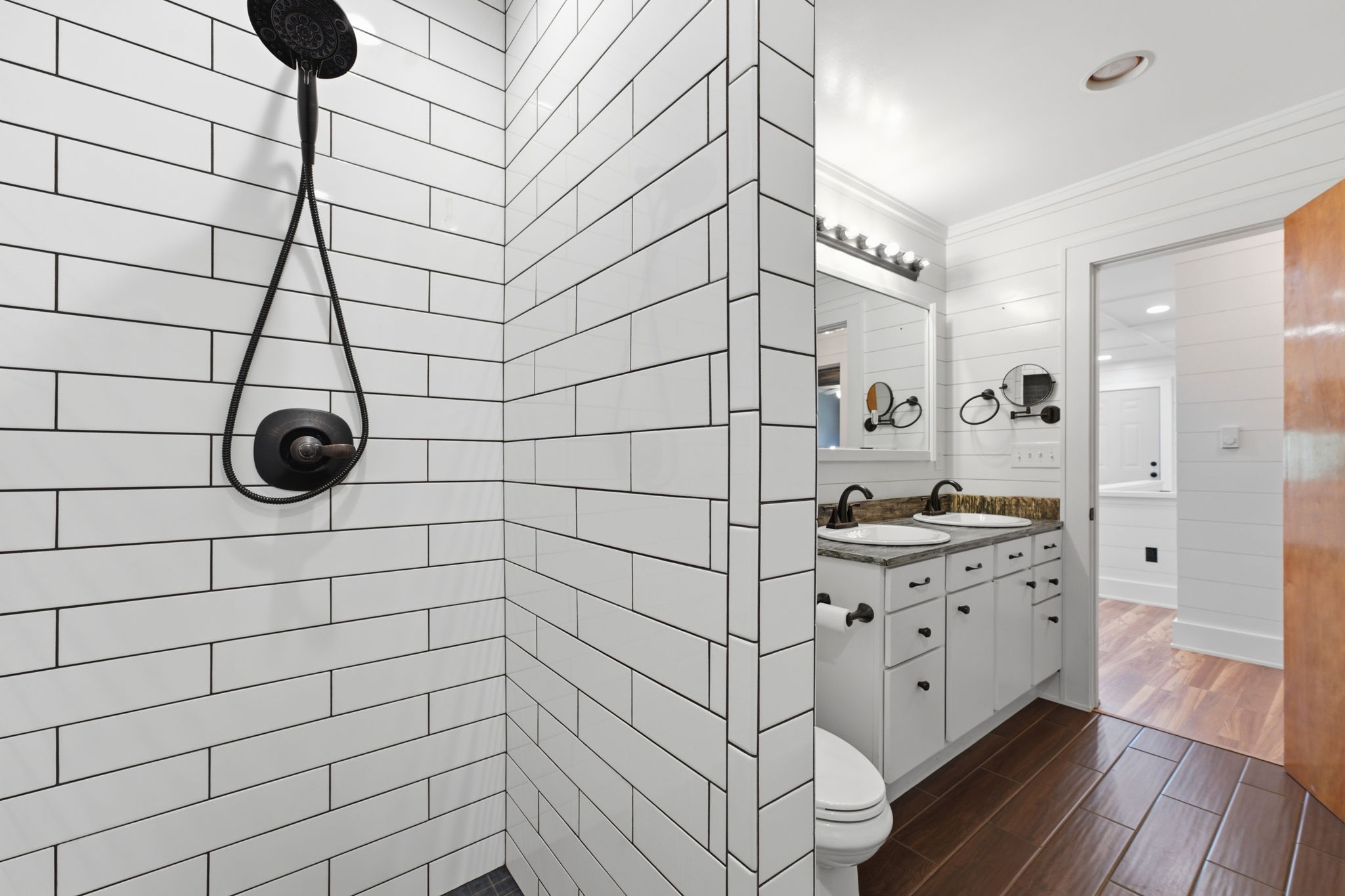Bathroom with a white subway-tile shower, black fixtures, double vanity, and dark tile floor.