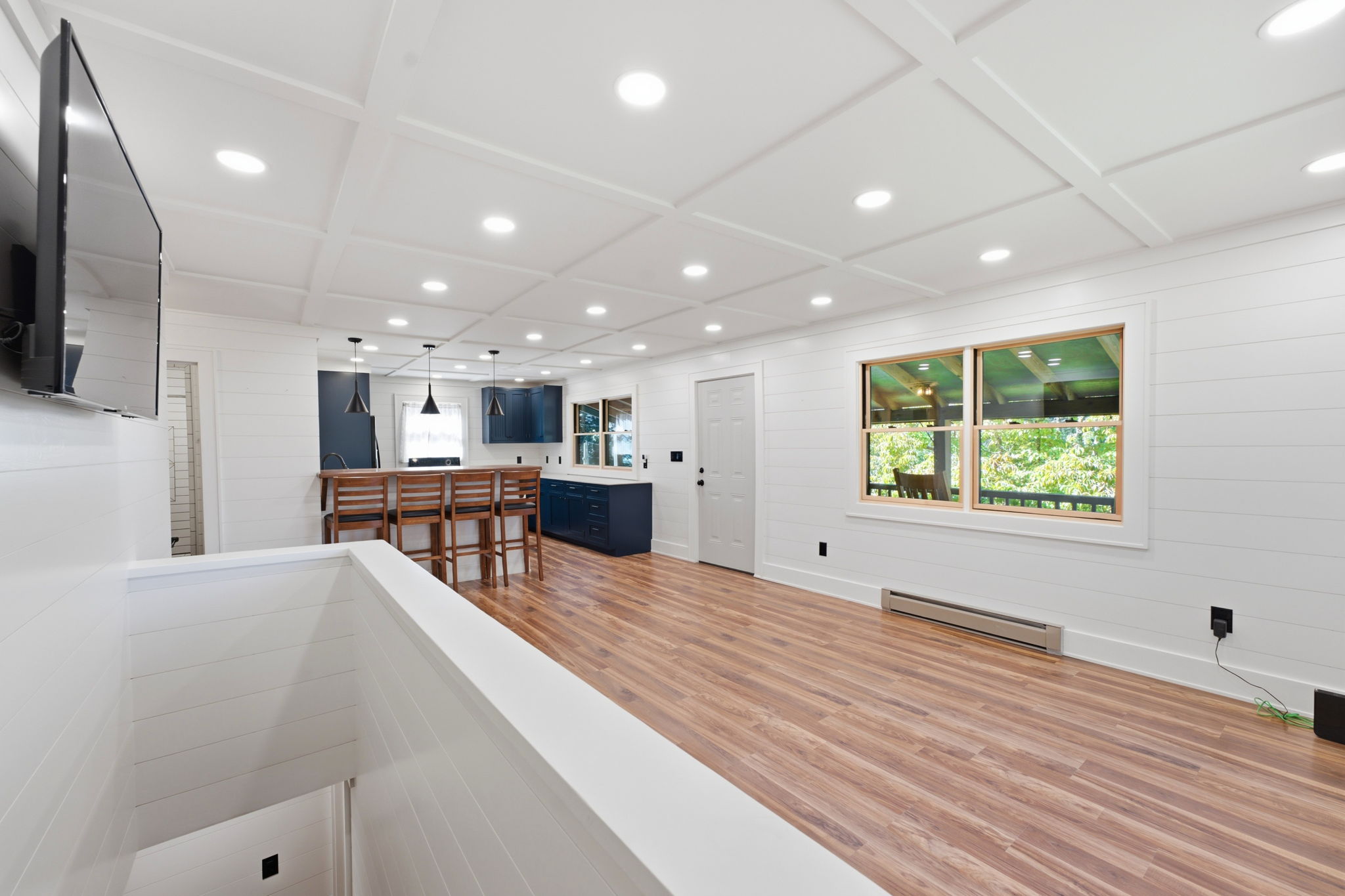 Open kitchen and living area with navy cabinets, wood floors, and a coffered ceiling.