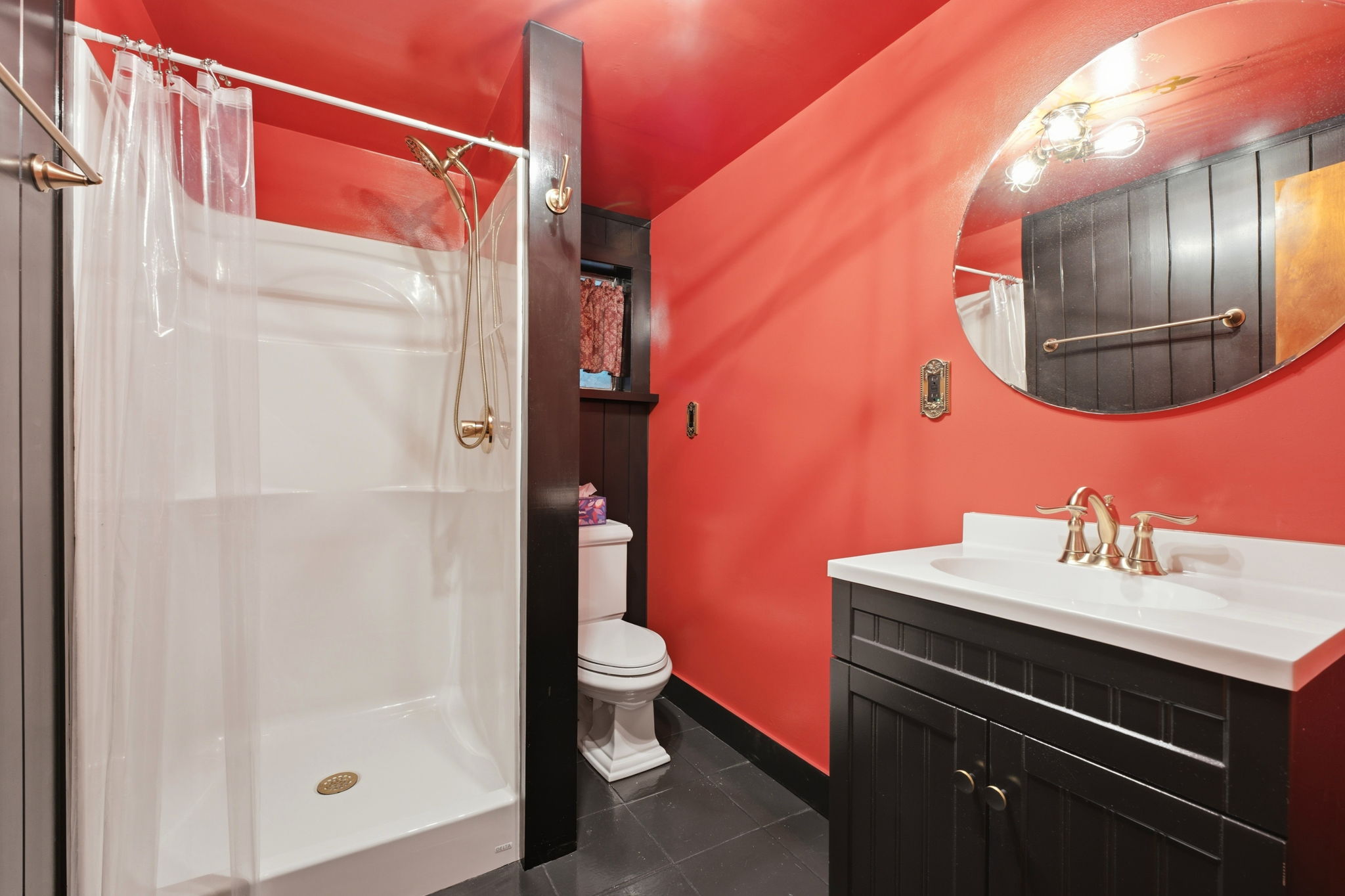 Bathroom with vivid red walls, black vanity, white shower, and large round mirror.