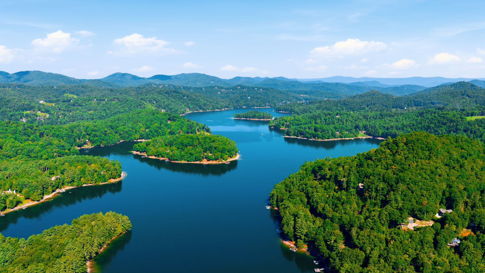 Aerial view of a winding lake among forested shores and distant mountain ridges.