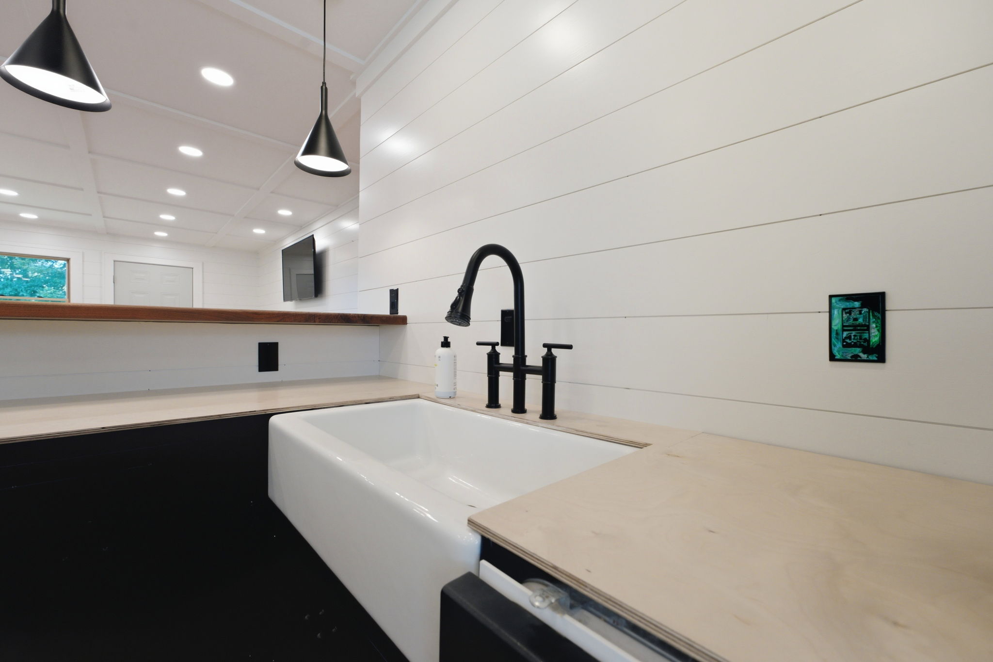 Kitchen sink with a white apron-front basin, black faucet, and pale wood countertops.