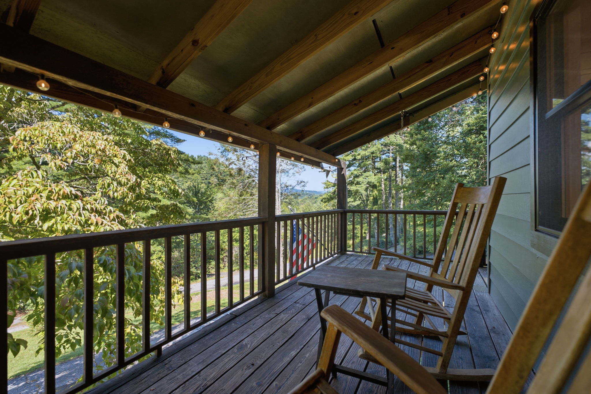 Covered wooden porch with rocking chairs and string lights overlooking a wooded mountain view.