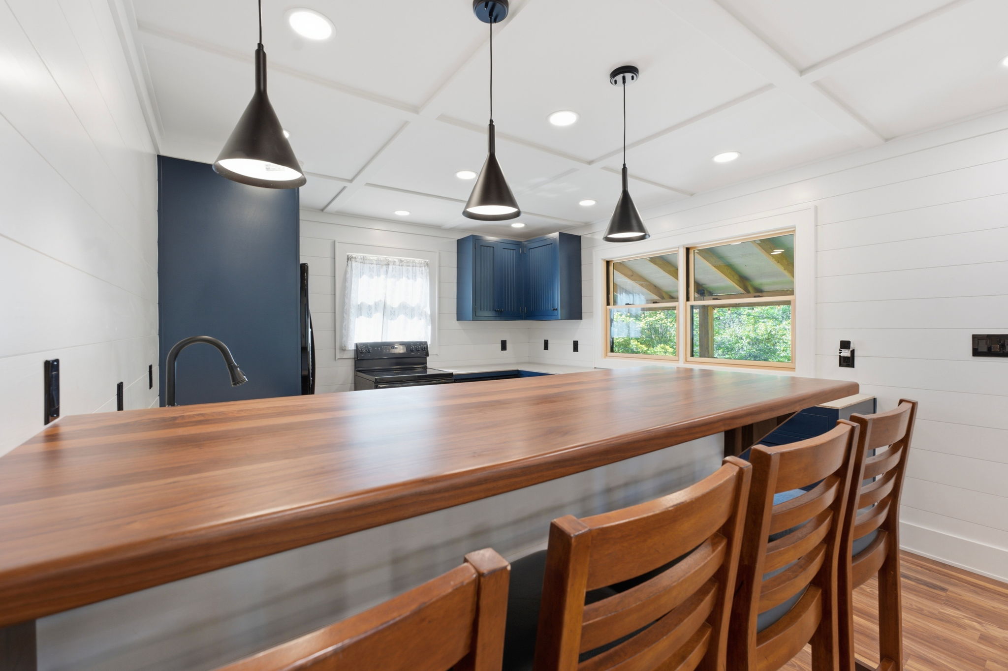 Kitchen with a long wood-topped breakfast bar, wooden stools, navy cabinets, and black pendant lights.