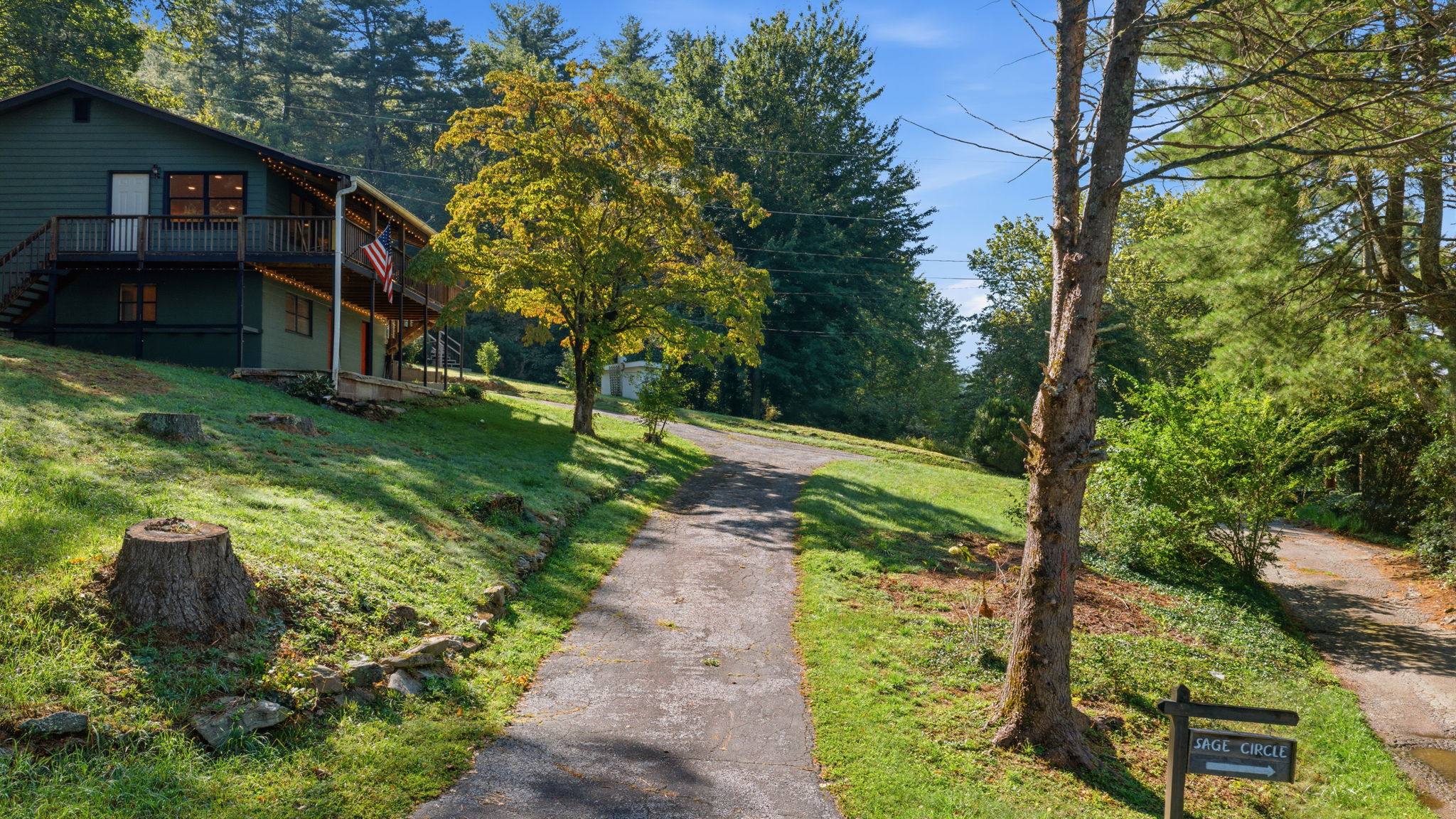 Dark green two-story house with a raised deck beside a curving driveway and Sage Circle sign.