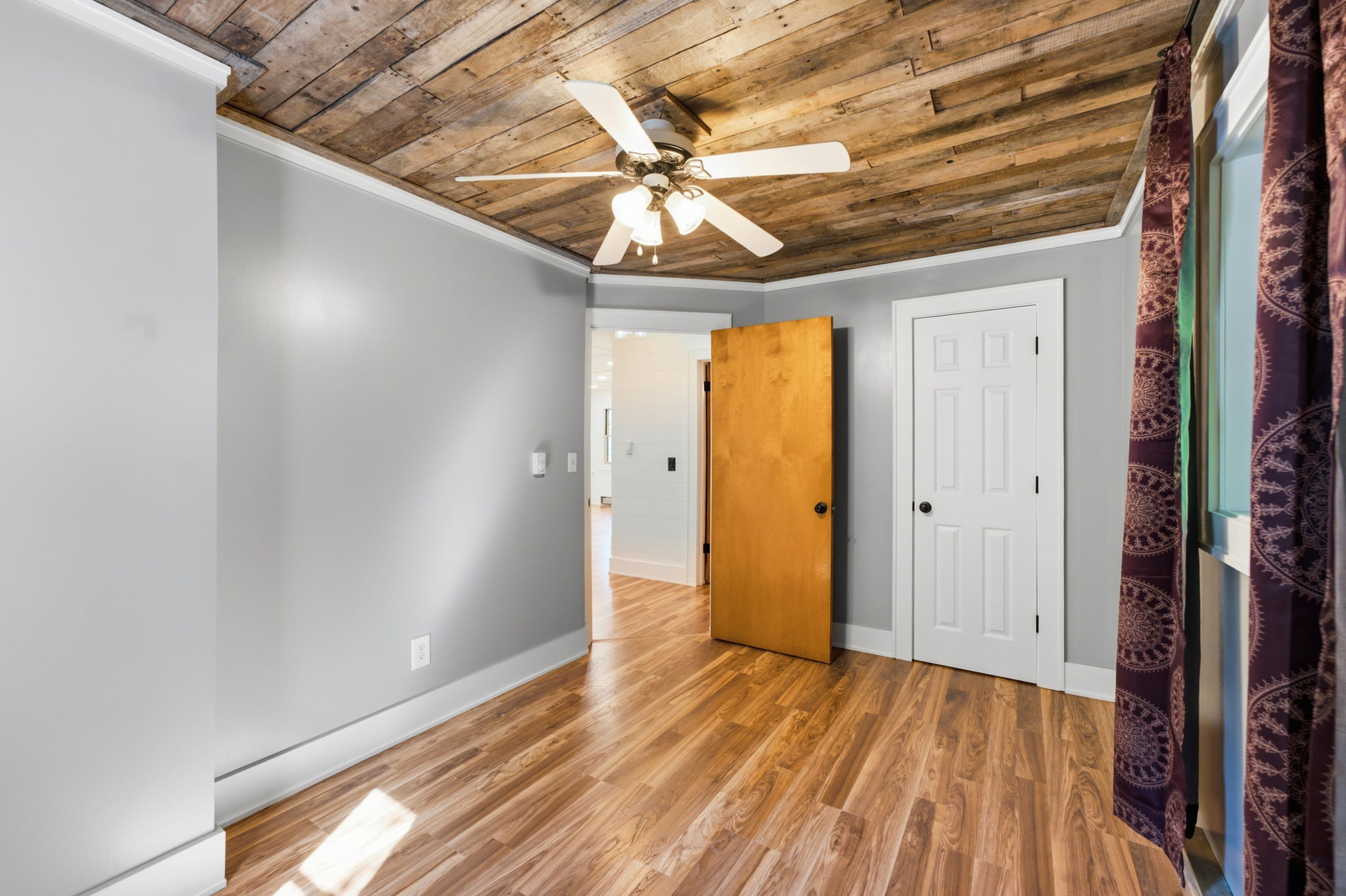 Room with a rustic plank ceiling, wood floors, and an open door to a bright adjoining space.