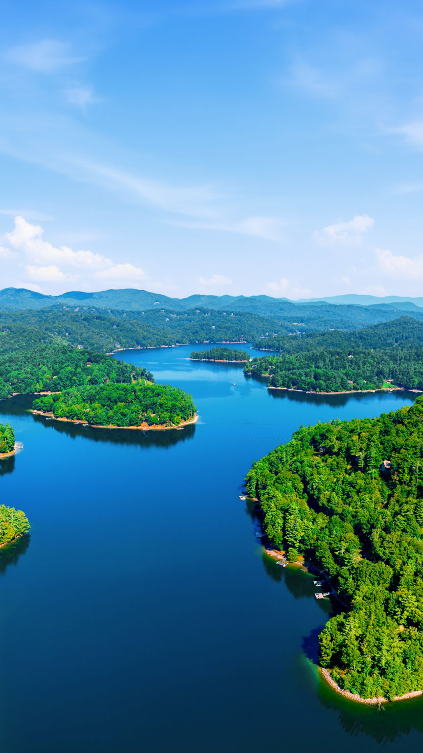 Aerial view of a blue lake winding through forested hills under a bright sky.