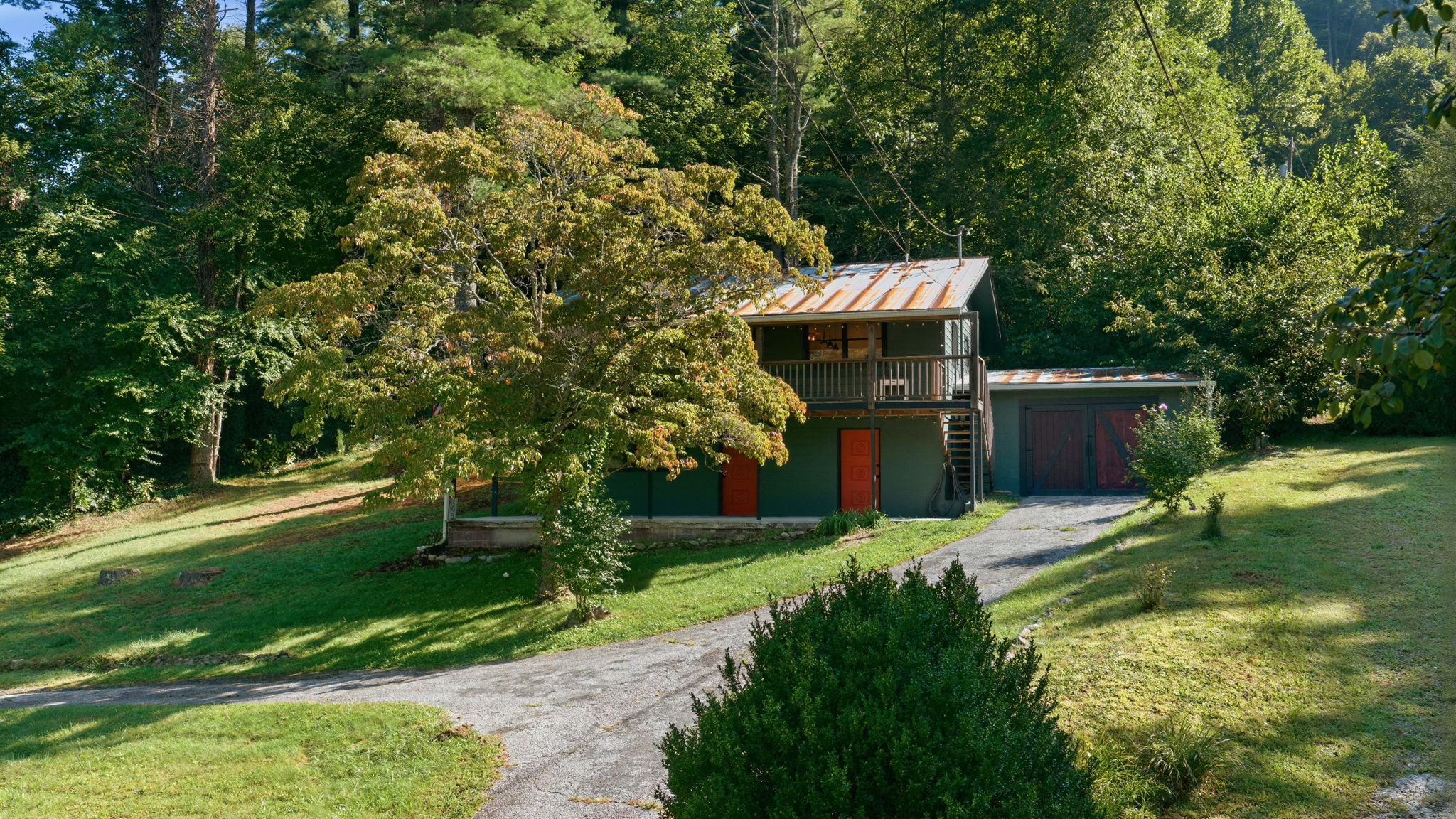 Wooded home with a rusted metal roof, upper deck, and detached garage.
