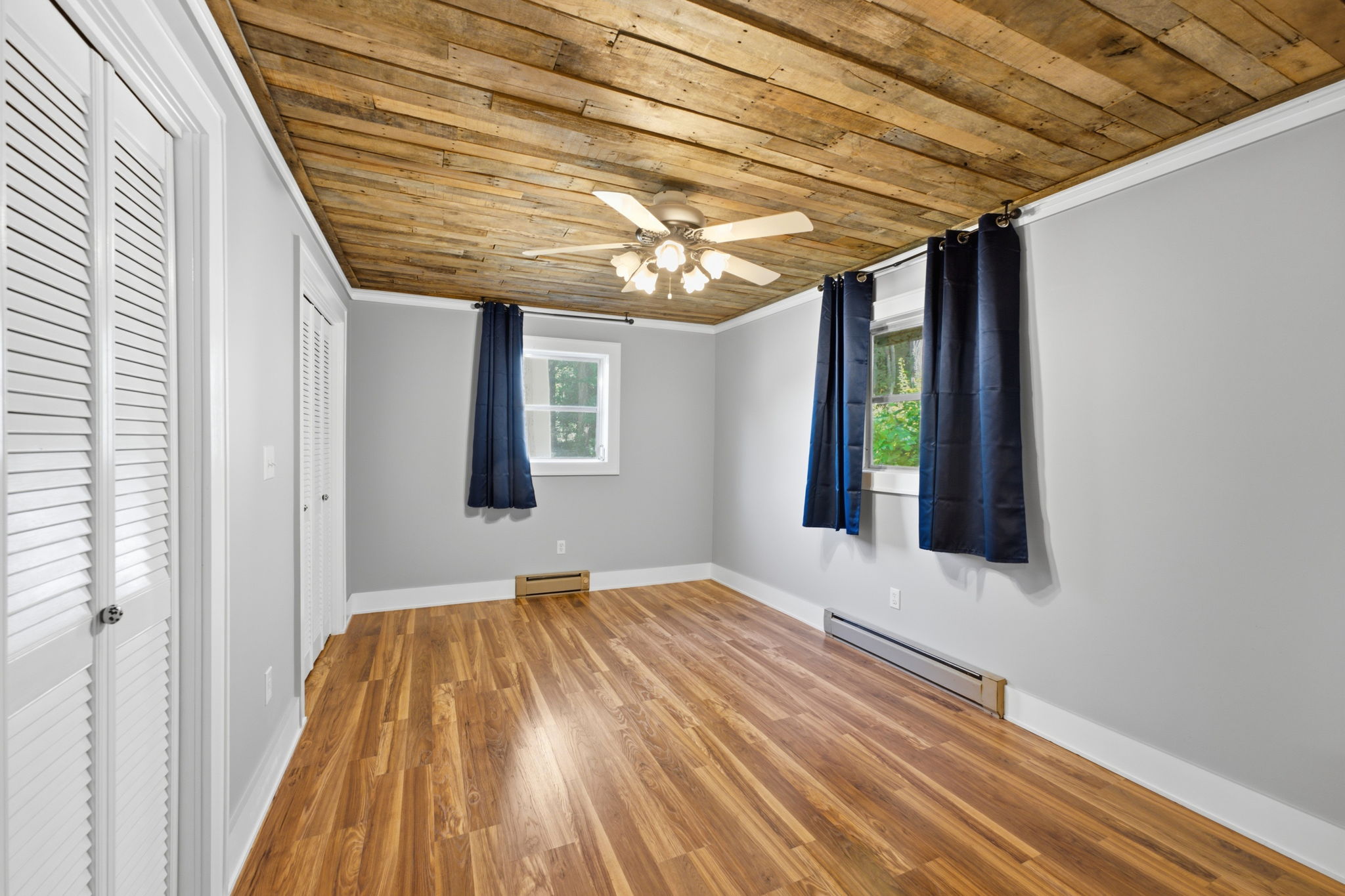 Empty bedroom with a rustic wood-plank ceiling, wood flooring, and navy curtains.