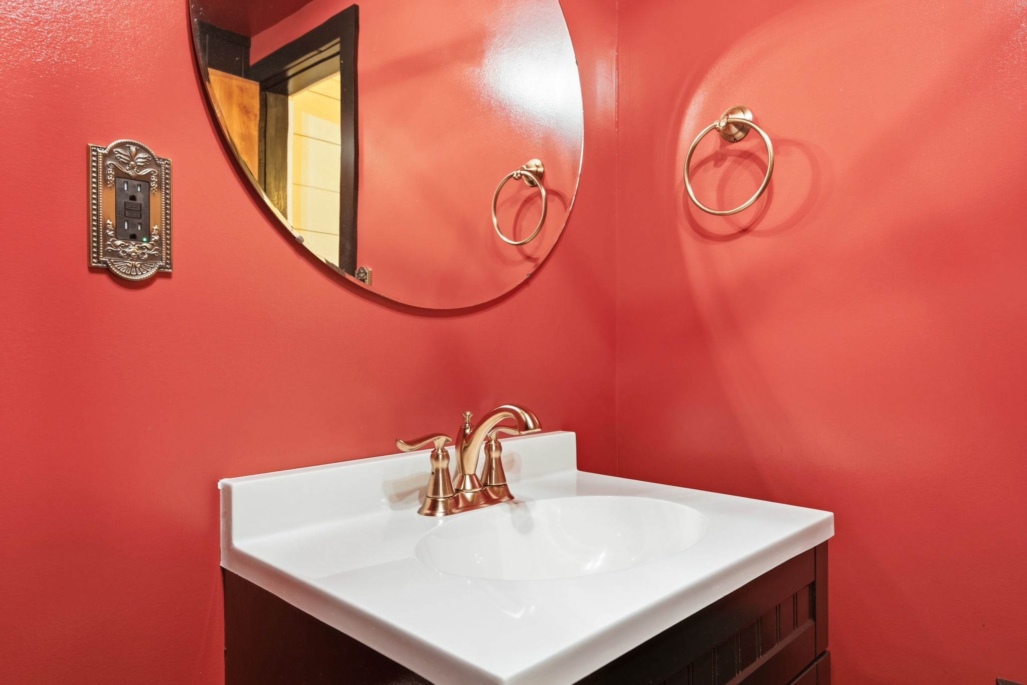 Bathroom vanity with a white sink, brass fixtures, round mirror, and vivid red walls.