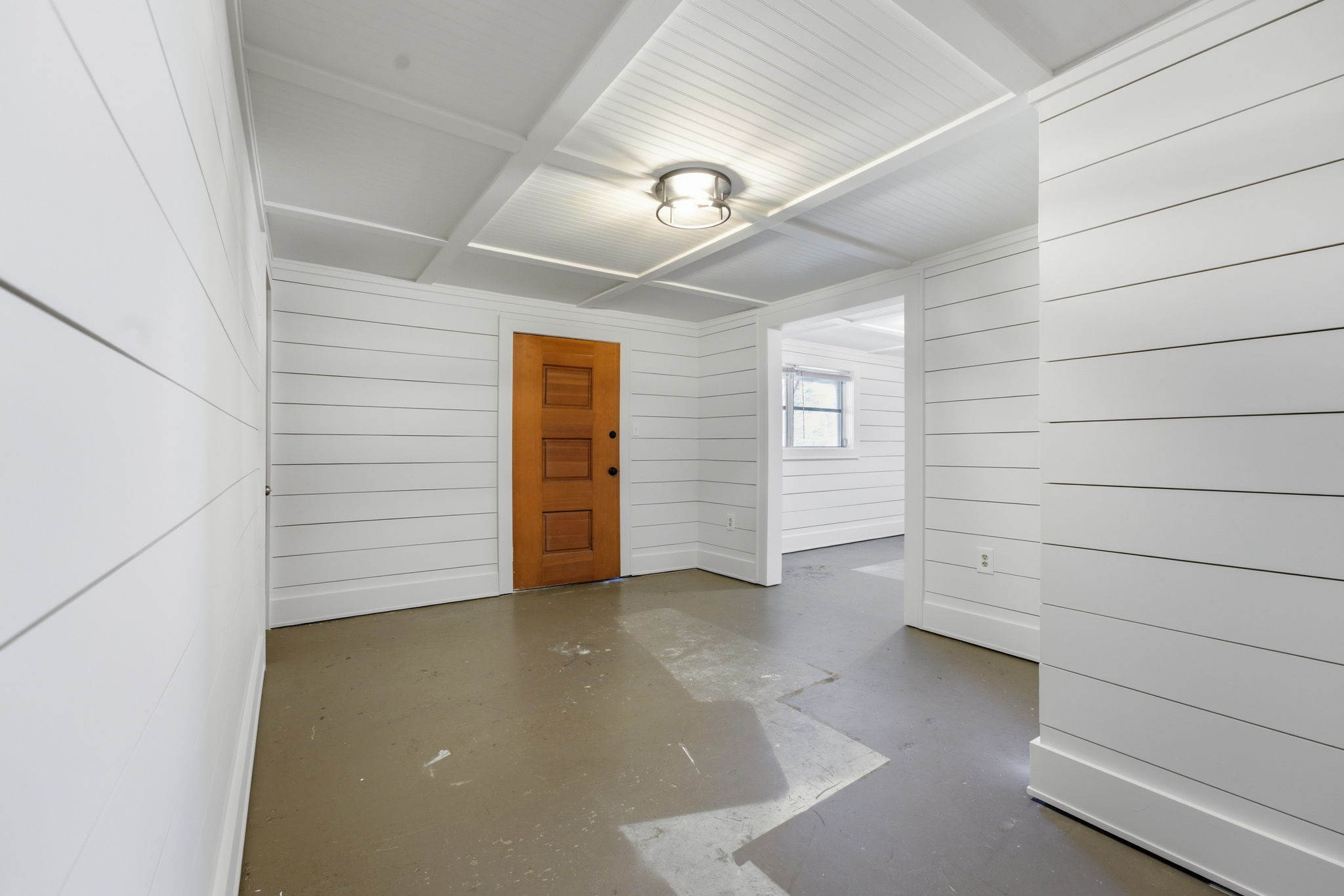Empty entry hall with white plank walls, a paneled wood door, and a concrete floor.