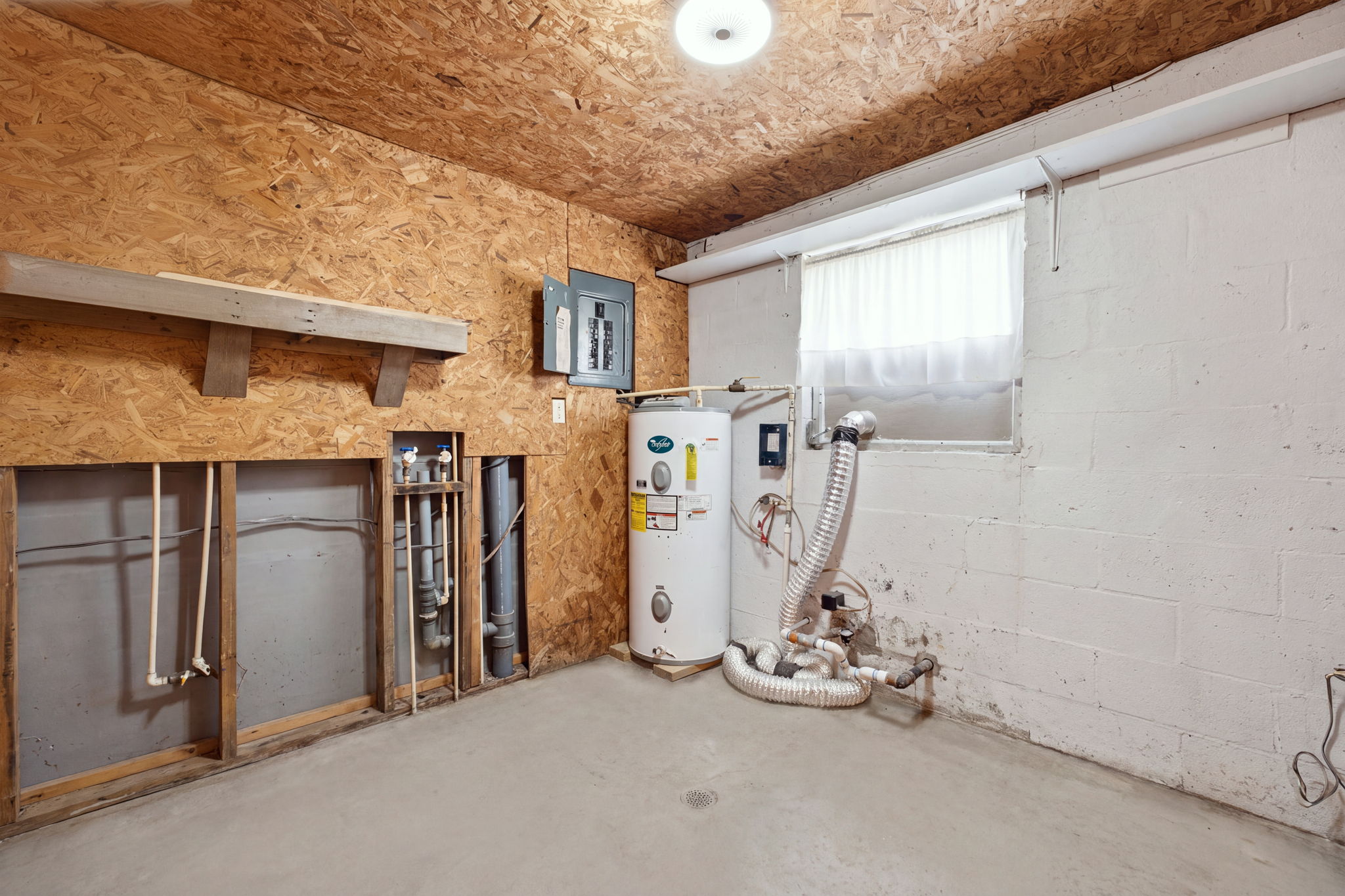 Basement utility room with a water heater, exposed plumbing, and an electrical panel.