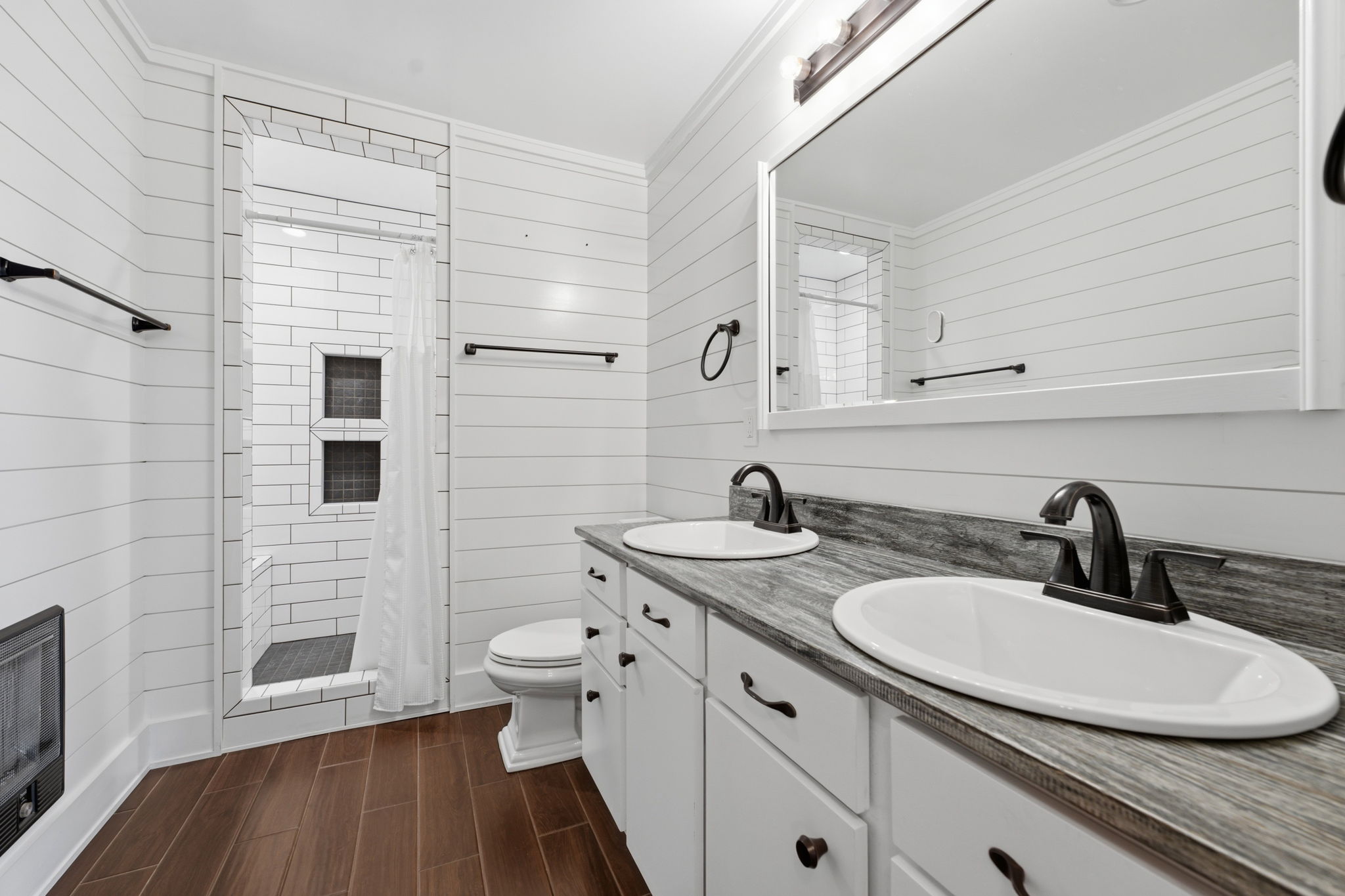 Bathroom with a double-sink vanity, white shiplap walls, and a tiled walk-in shower.
