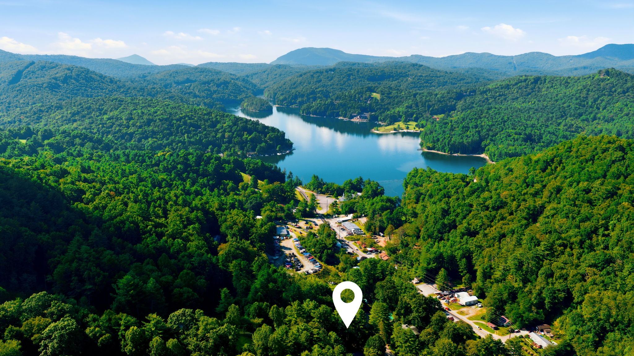 Aerial view of a mountain lake surrounded by forest, with a white location marker in the foreground.
