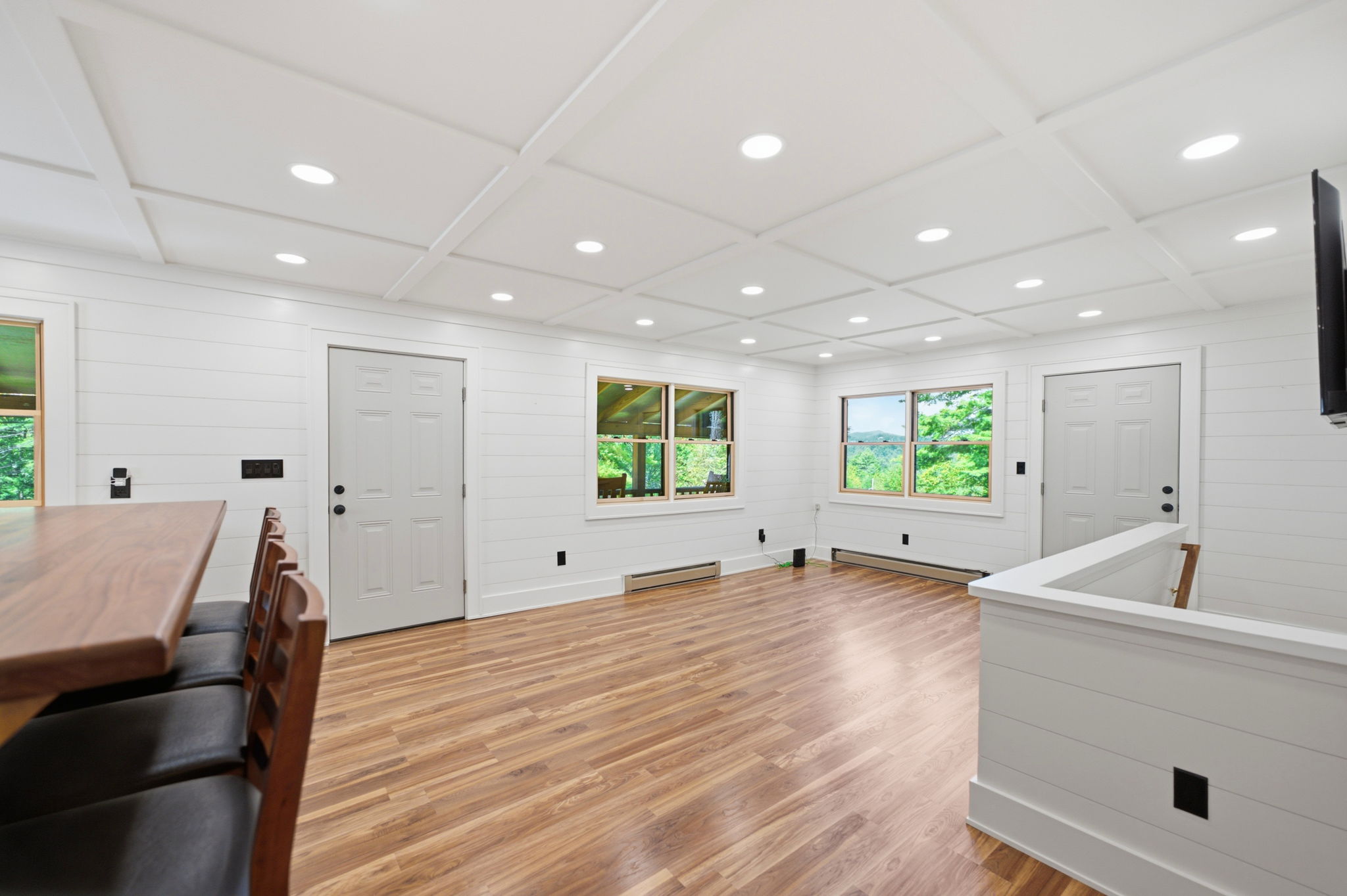 Upstairs living area with a coffered ceiling, wood-look floors, and windows facing trees.