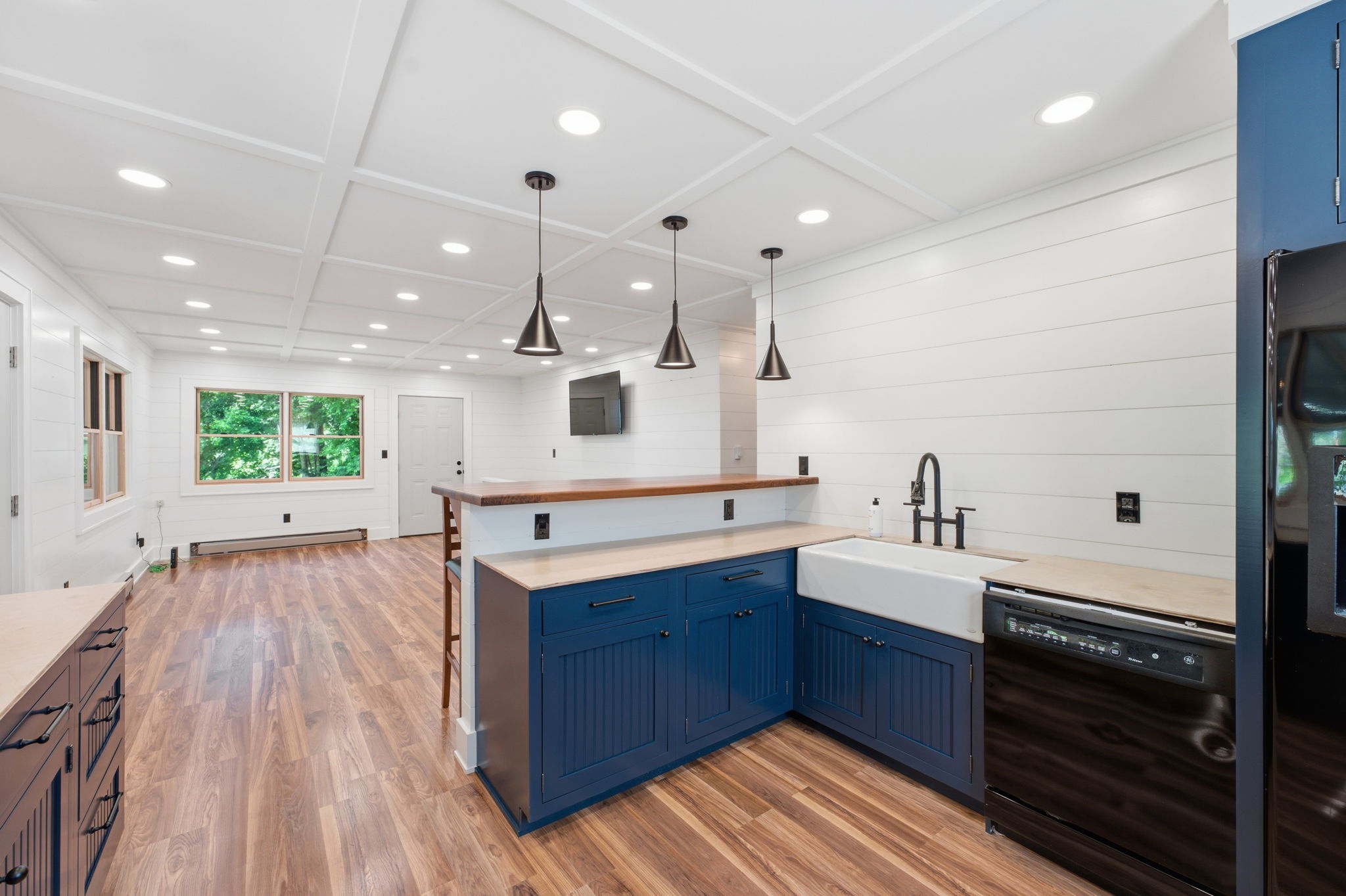 Kitchen with navy cabinets, farmhouse sink, wood-topped island, and coffered ceiling.
