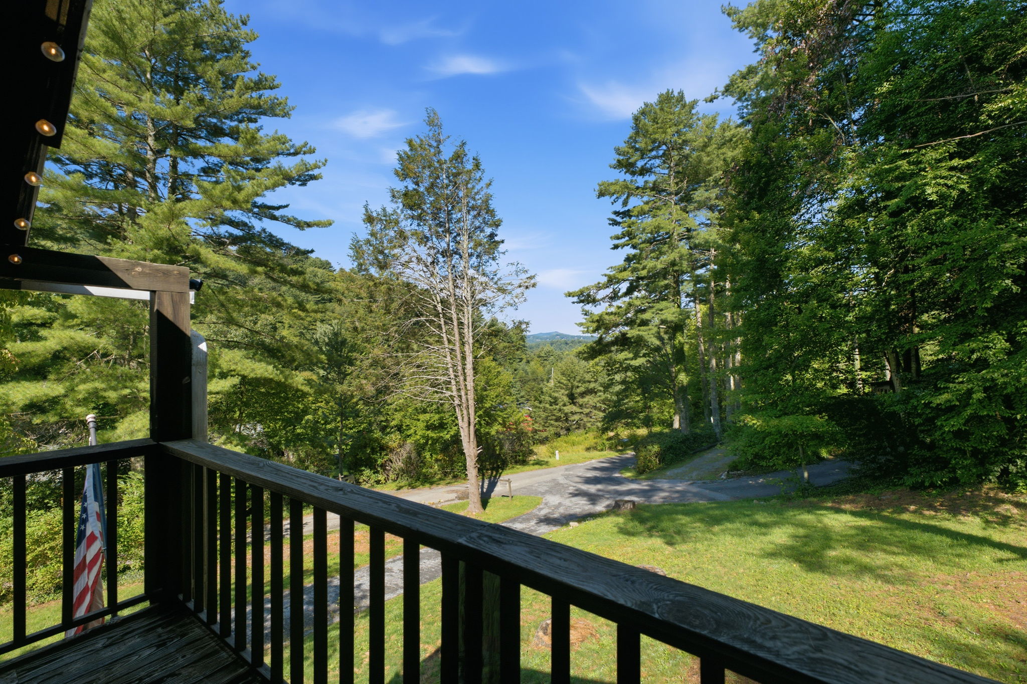 Porch overlooks a wooded yard, winding road, and distant mountain ridge.