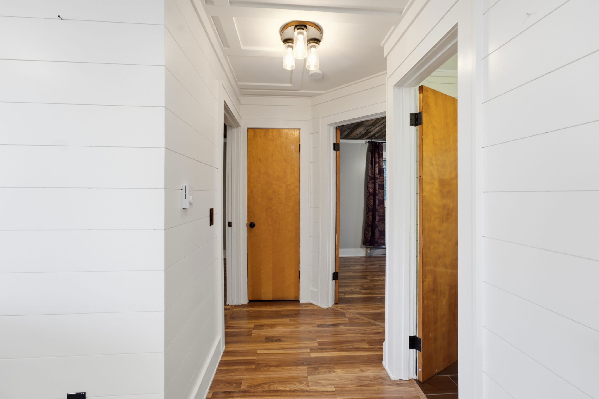 Hallway with white plank walls, wood-look flooring, a tray ceiling and open wooden doors.