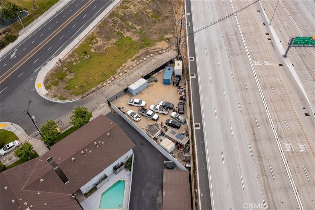 Aerial view of the property beside a freeway, with a swimming pool and fenced vehicle yard.