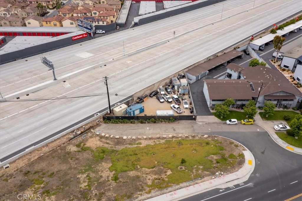 Vacant corner lot beside a freeway, with nearby buildings and a vehicle yard.
