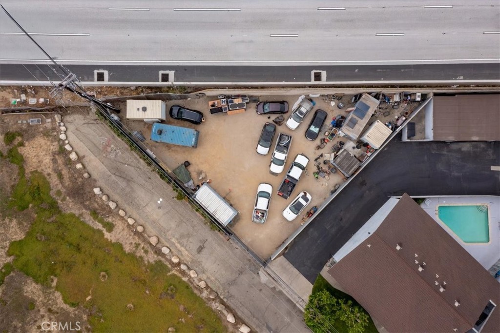 Aerial view of a dirt lot with parked cars and trailers beside a neighboring home and pool.