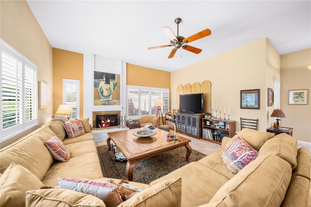 Living room with tan sofas, a lit fireplace, white shutters, and a wooden coffee table.