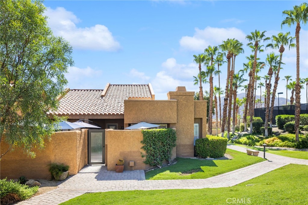 Tan stucco home with a tiled roof, palm trees, and a curved walkway through the lawn.