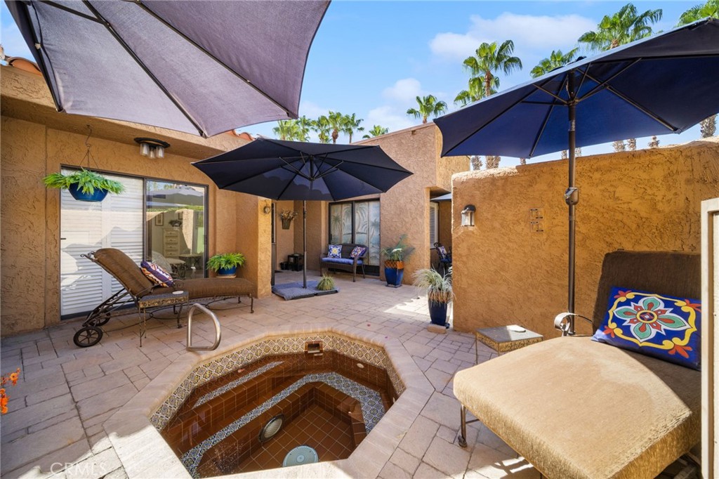 Private courtyard patio with a tiled spa, shaded lounge seating, and palm trees.