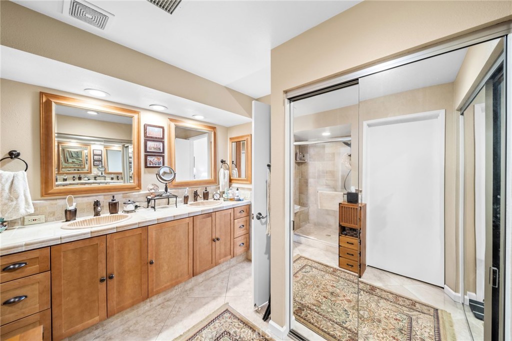 Bathroom with a long wood double vanity, framed mirrors, and a glass-enclosed shower.