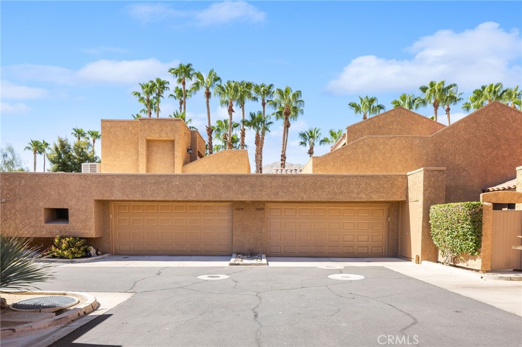 Tan stucco residence with two garage doors and palm trees behind the roofline.