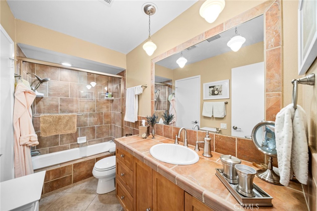 Bathroom with a tiled tub and shower, wood vanity, and large wall mirror.