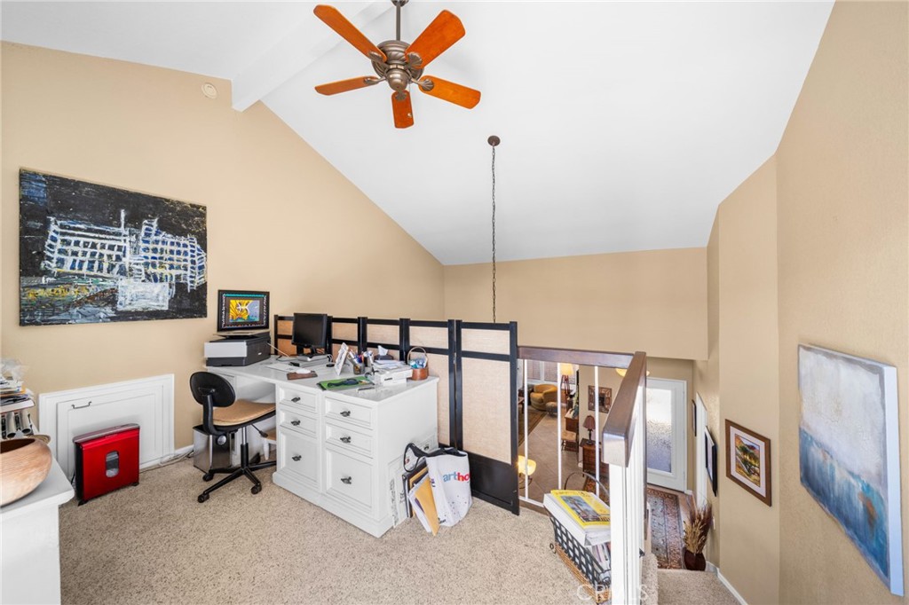 Upstairs loft office with a white desk, black railing, and orange-bladed ceiling fan.