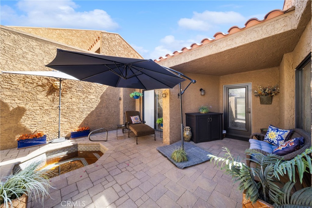 Enclosed courtyard patio with a large umbrella, cushioned seating, potted plants, and a small tiled water feature.