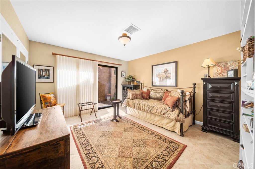 Bedroom with a patterned daybed, large rug, dark dresser, and sliding glass door.