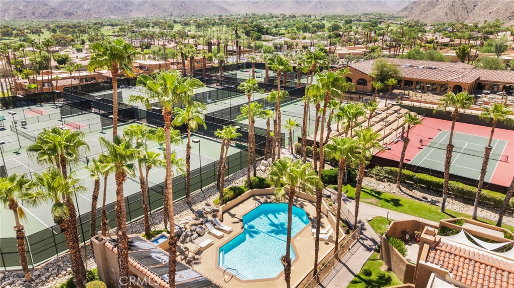 Aerial view of a palm-lined community pool and multiple tennis courts with mountains beyond.