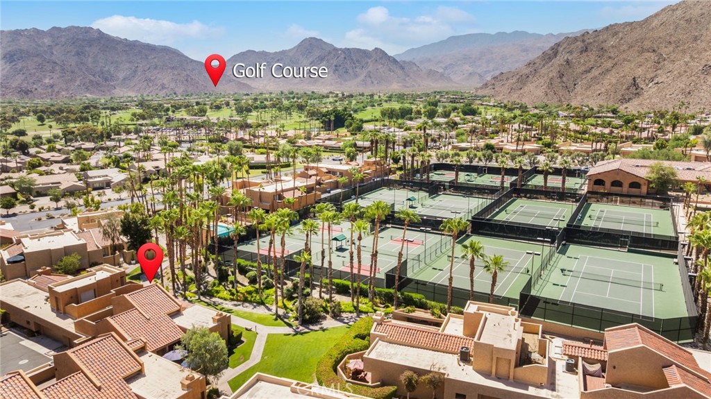 Aerial view of homes and tennis courts beside a golf course, with mountains in the background.