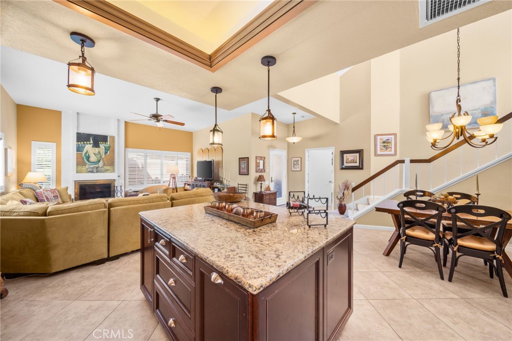 Open-plan kitchen and living area with granite island, fireplace, dining table, and raised ceiling.