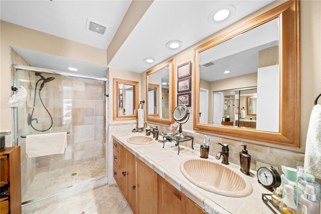Bathroom with a glass-enclosed tiled shower and a double-sink vanity beneath large wood-framed mirrors.