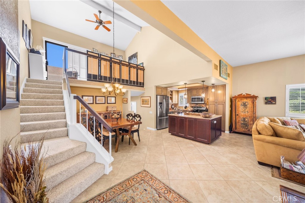Open-plan living area with a carpeted staircase, loft railing, dining table, and kitchen island.