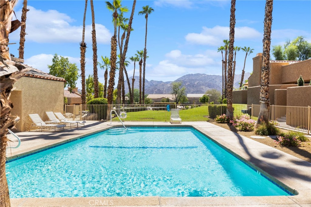 Swimming pool framed by palm trees, with lounge chairs and mountains in the distance.