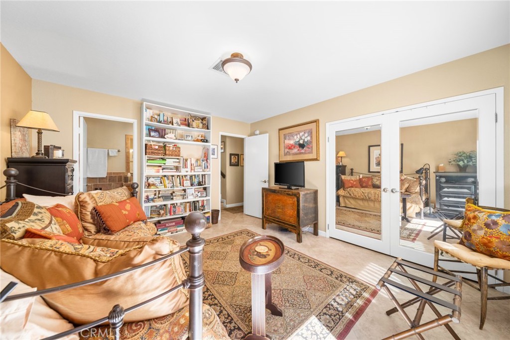 Bedroom with patterned orange bedding, a full bookcase, and French doors opening to a sitting area.