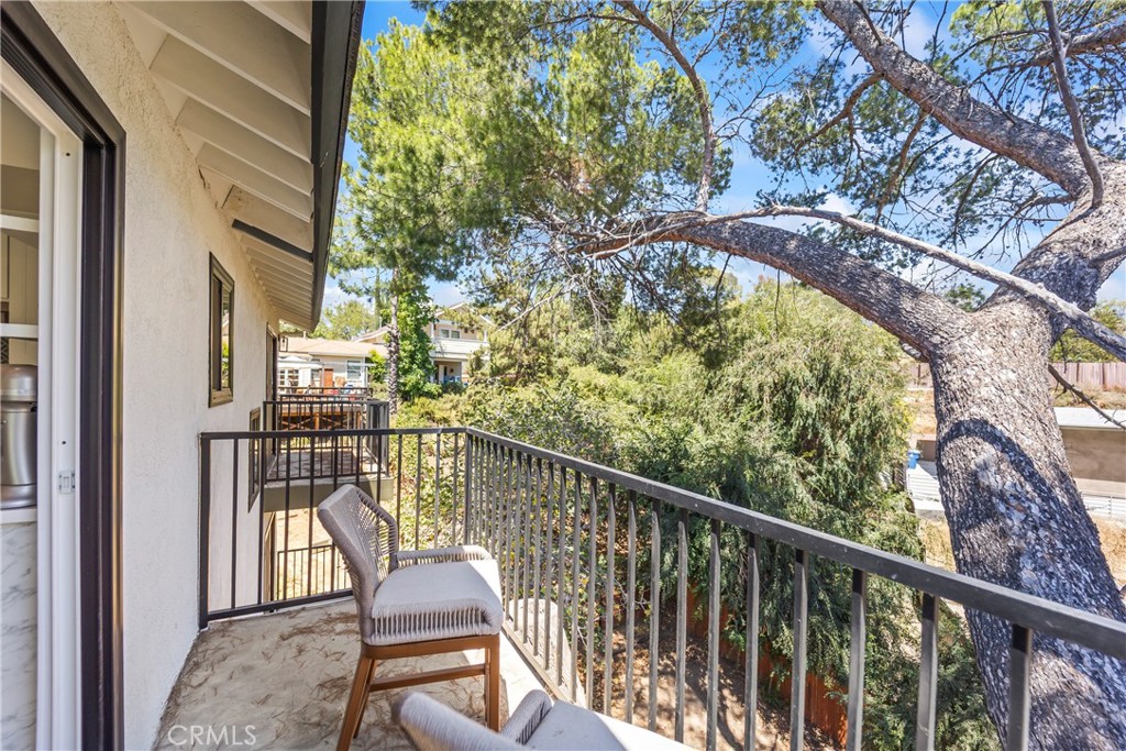 Furnished balcony with black metal railing and chairs overlooking leafy trees beneath a large spreading tree.